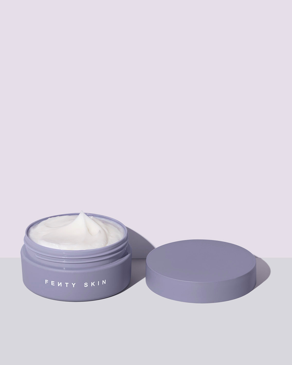 An open tub of a travel size Butta Drop Whipped Oil Body Cream with Tropical Oils + Shea Butter on a lilac background.